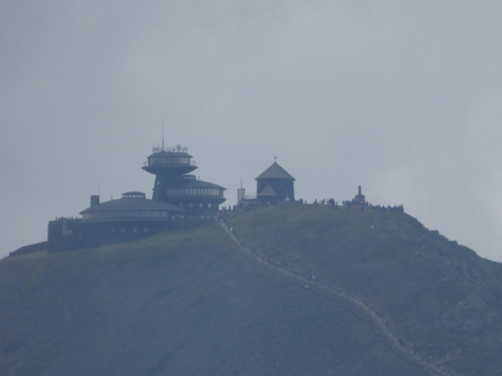 Śnieżka Widok na Śnieżkę. Nieco zamglony horyzont, z lewej schronisko z prawej nieduża drewniana kaplica.